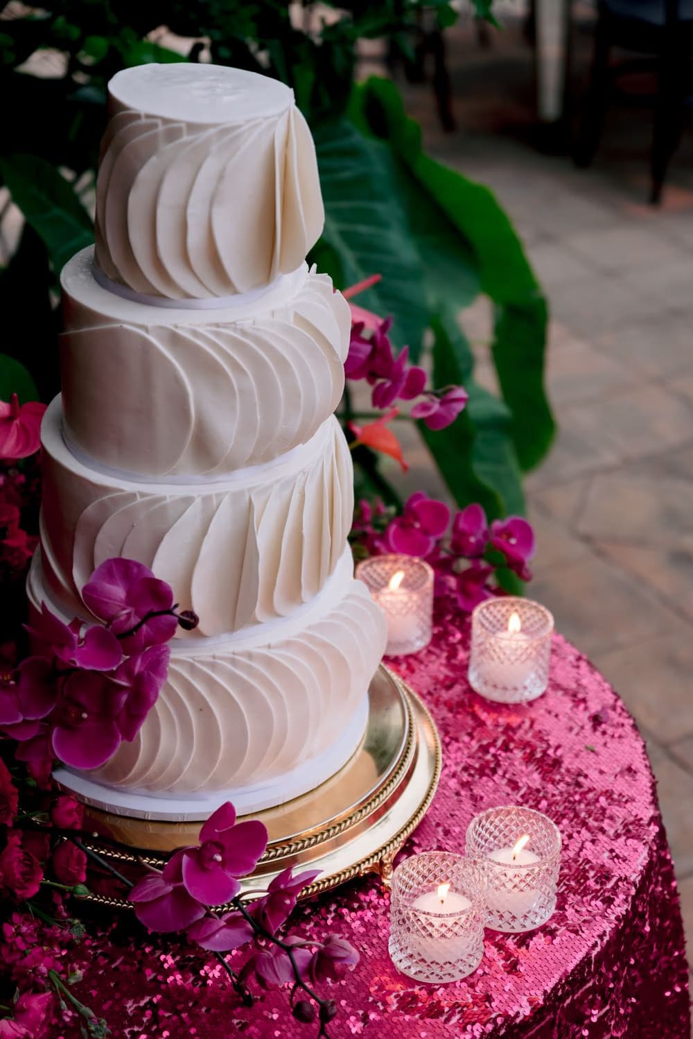 Four-tier ruffled wedding cake with magenta orchids on a pink sequined linen — vibrant reception detail.