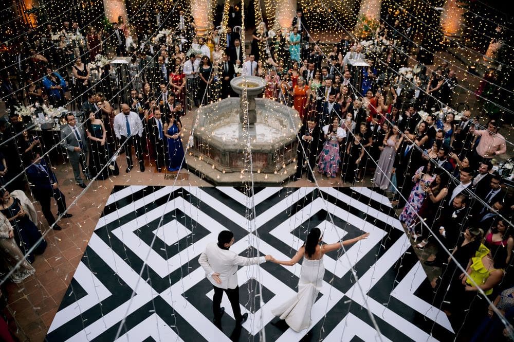 Symmetric mirrored aerial shot of the couple's first dance on the geometric dance floor at the courtyard reception.