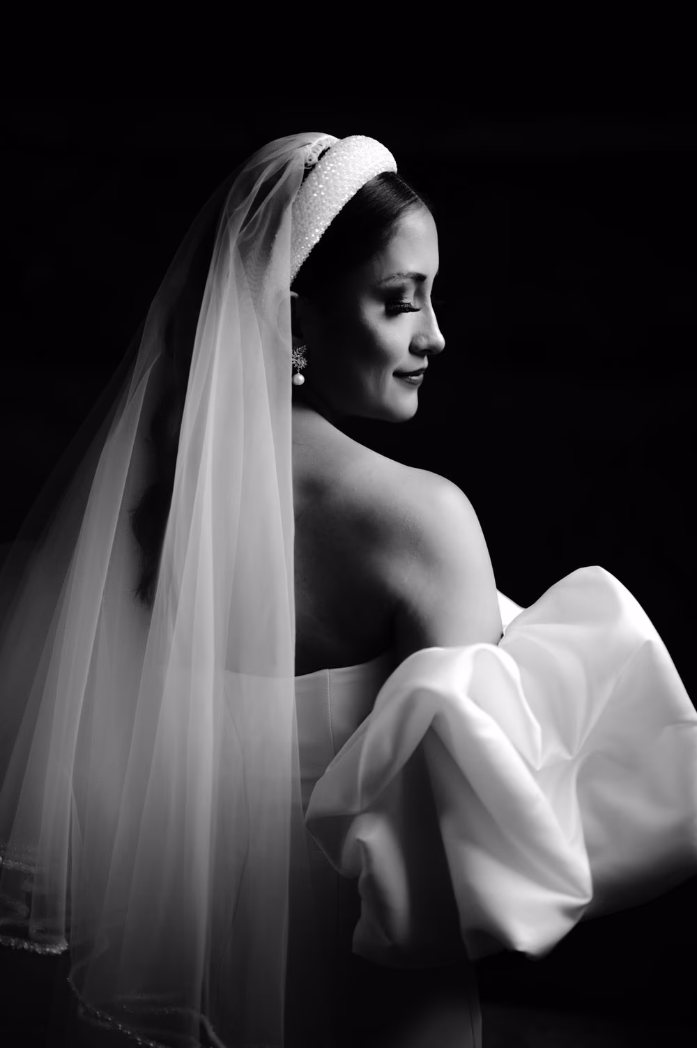 Black-and-white editorial portrait of bride Andrea in puff-sleeve gown, crystal headband and cathedral veil, glancing over her shoulder at Capuchinas Ruins in Antigua Guatemala.
