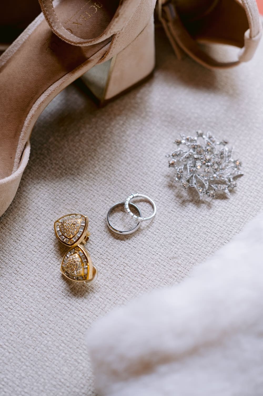 Bridal getting-ready details — gold heart earrings, paired wedding bands and crystal hair piece beside suede heels at Antigua Guatemala wedding.