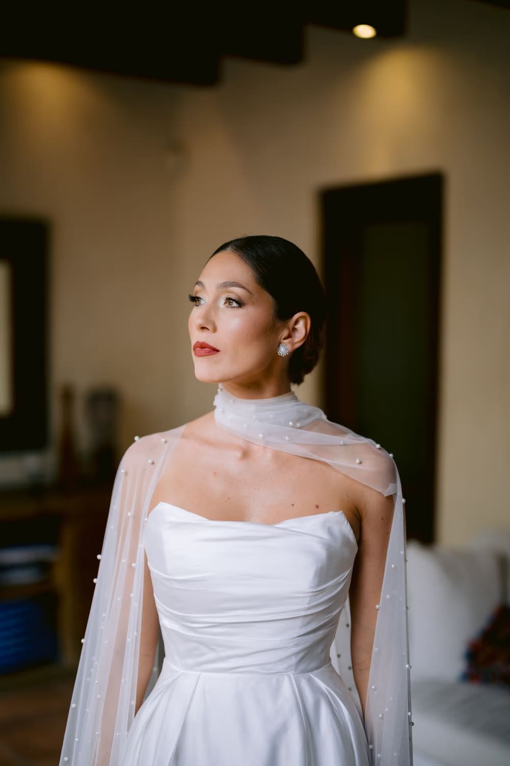 Soft daylight bridal portrait — satin bodice, pearl cape and red lip in the hotel suite before the ceremony in Antigua.