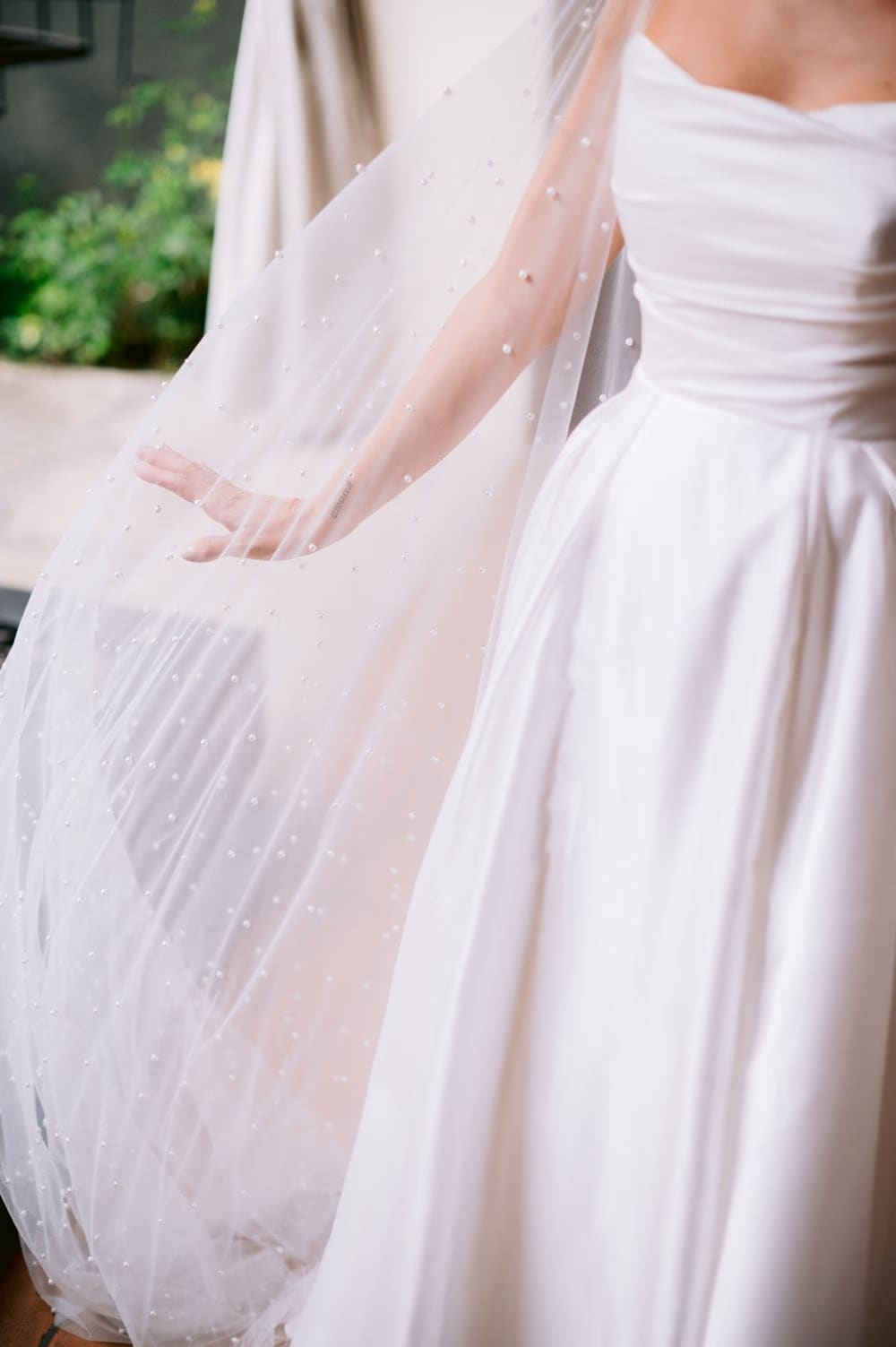 Detail of bride's hand lifting the pearl-studded tulle cape over her satin skirt — wedding gown shot at La Antigua.