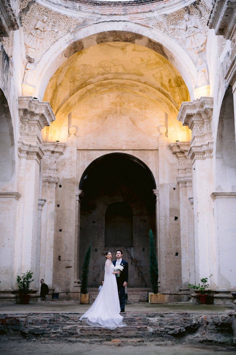 Bride and groom stand small beneath the soaring frescoed vault of Capuchinas Ruins — intimate destination wedding in Antigua Guatemala.