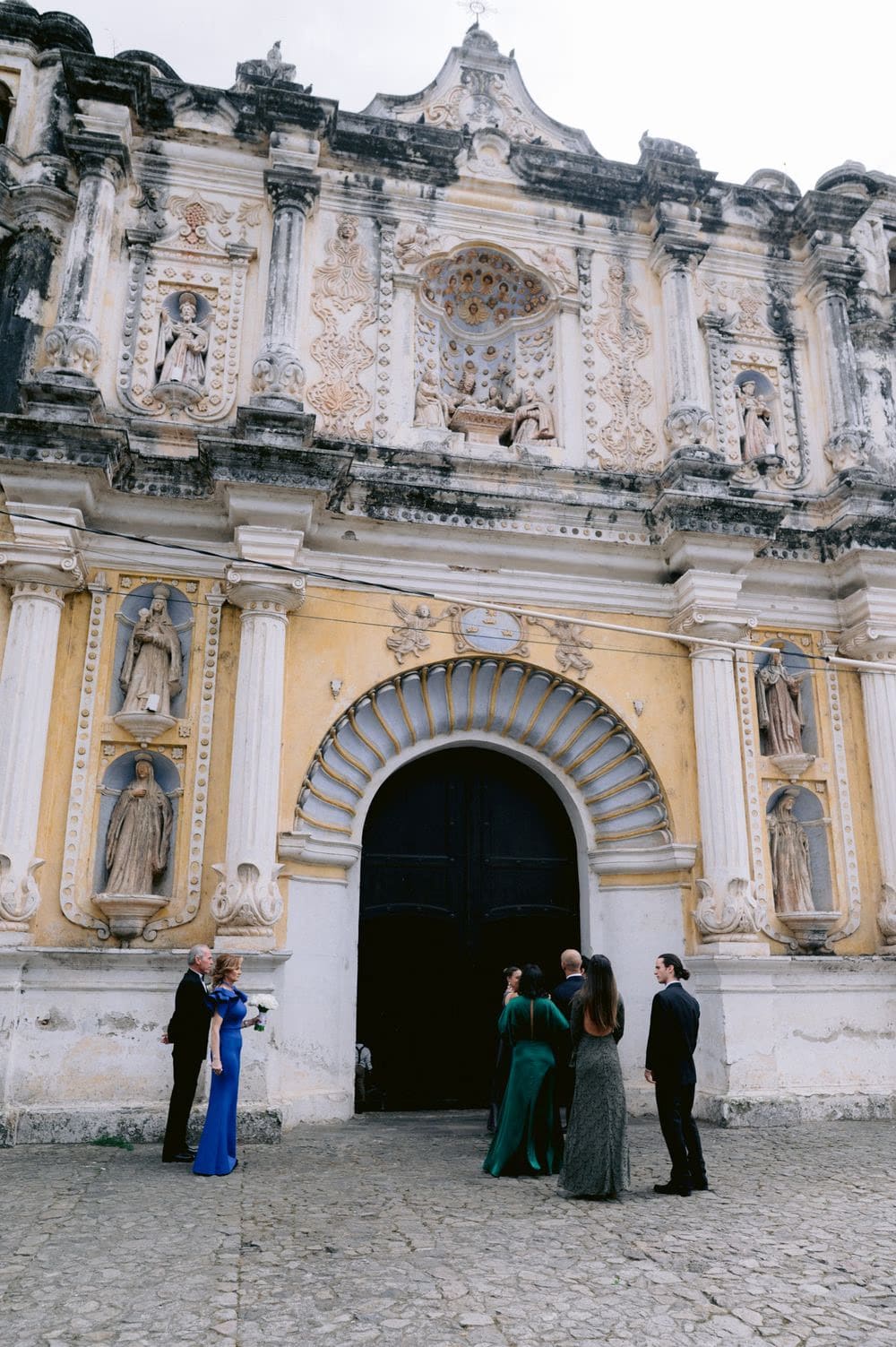 Guests gather outside the carved baroque facade of San Francisco church before the wedding ceremony in colonial Antigua.