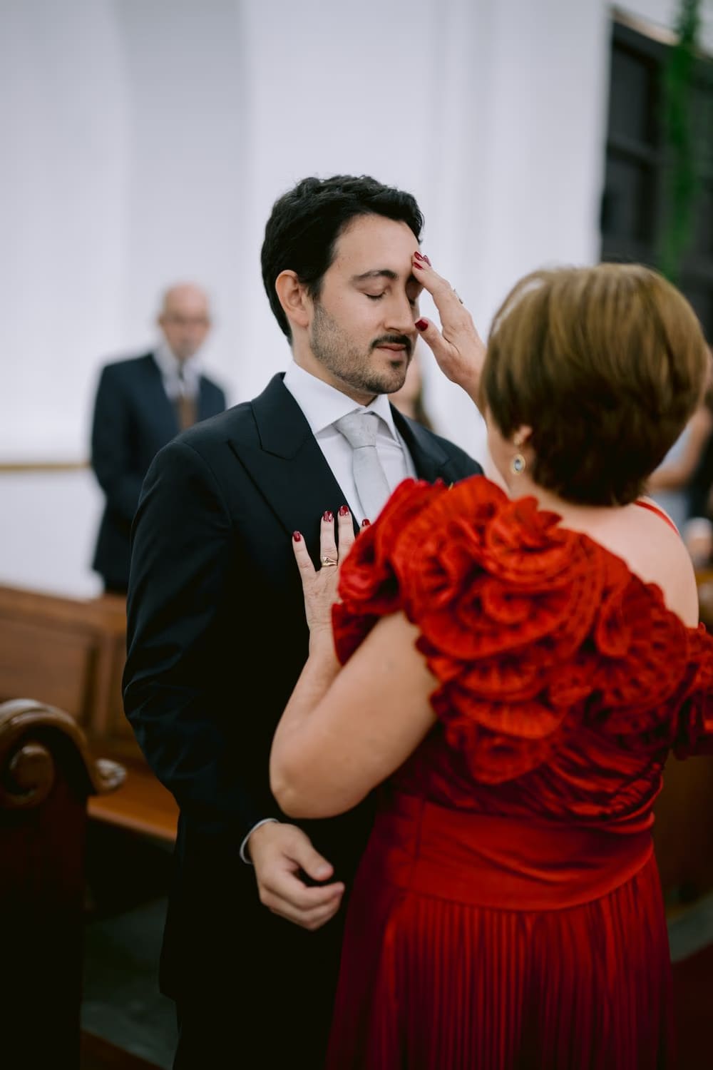 Mother of the groom in red blesses her son inside the church before the wedding ceremony — family wedding in Antigua.