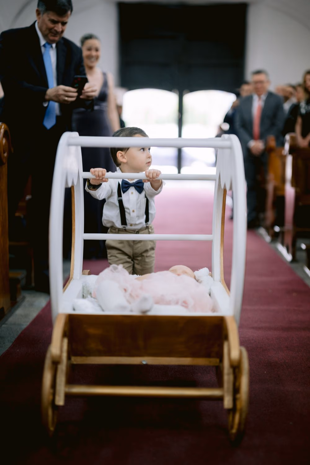 Toddler ring bearer in suspenders pushes a wooden cart down the church aisle — sweet family wedding moment in Antigua.