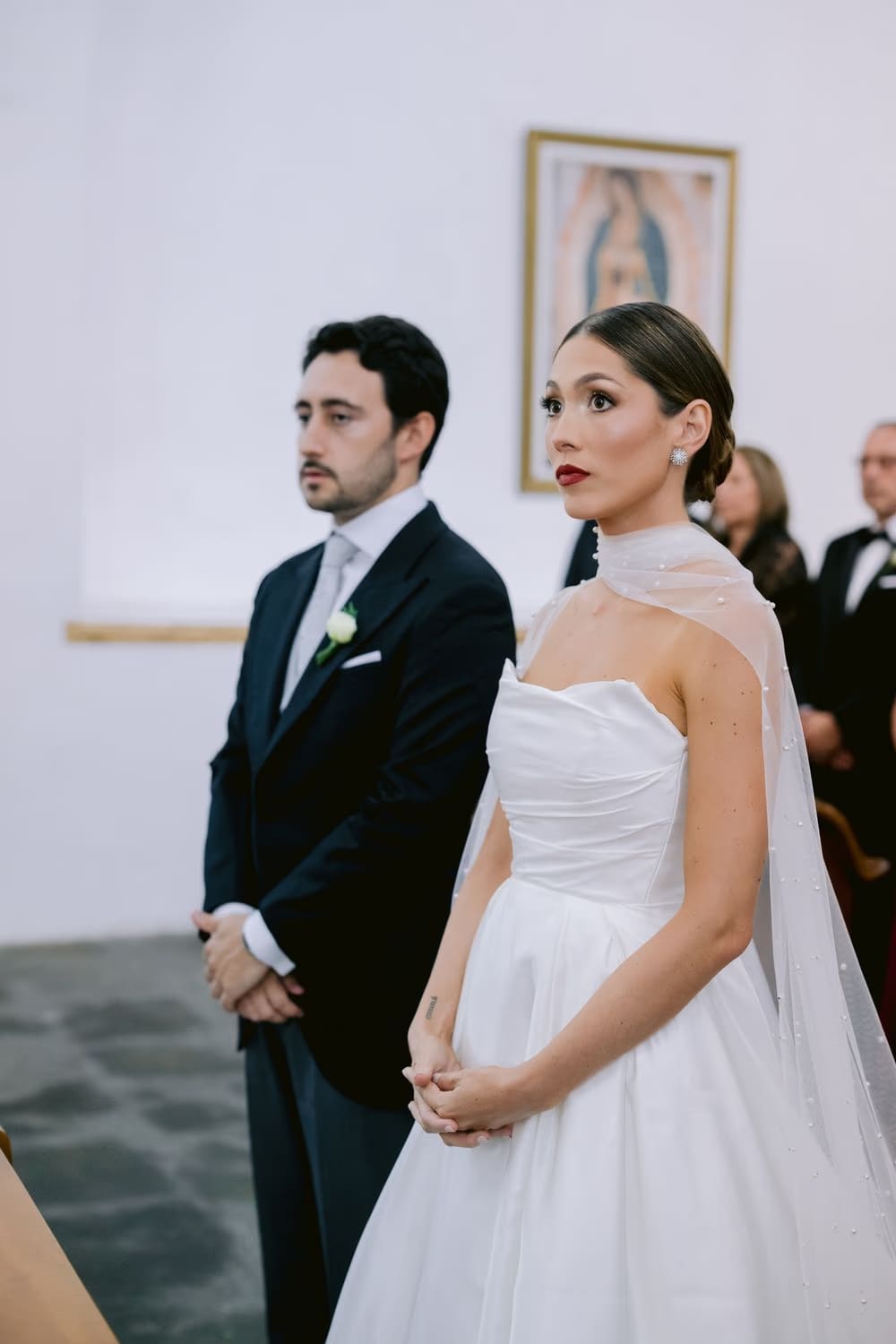 Couple stand together holding hands during the wedding ceremony, Guadalupe painting watching over them in Antigua Guatemala.