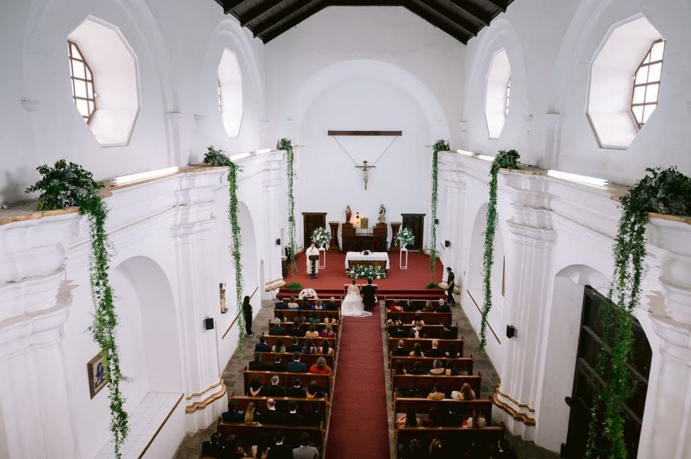 Wide view of the white-walled church with greenery garlands during the wedding ceremony in Antigua Guatemala.