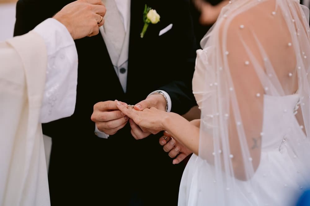 Priest places the wedding band on the bride's finger as the groom watches — ring exchange during the ceremony in Antigua Guatemala.