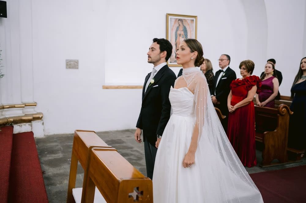 Bride and groom stand together before the Guadalupe painting flanked by their parents during the wedding ceremony.