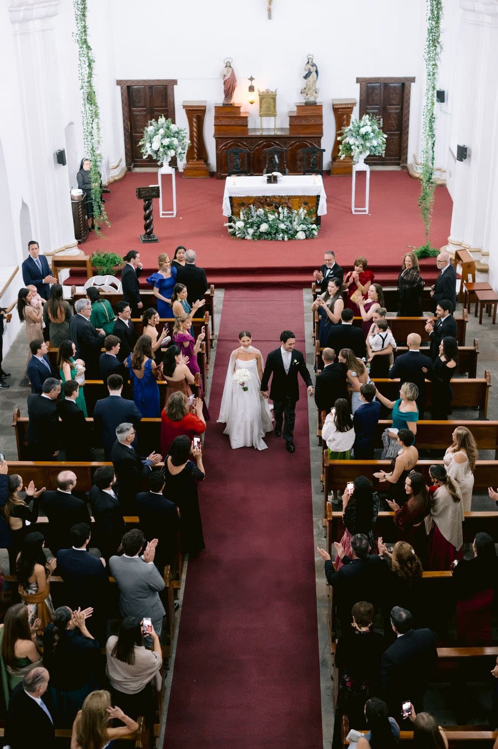 Overhead view as bride and groom recess down the aisle while guests applaud — wedding exit in colonial Antigua church.