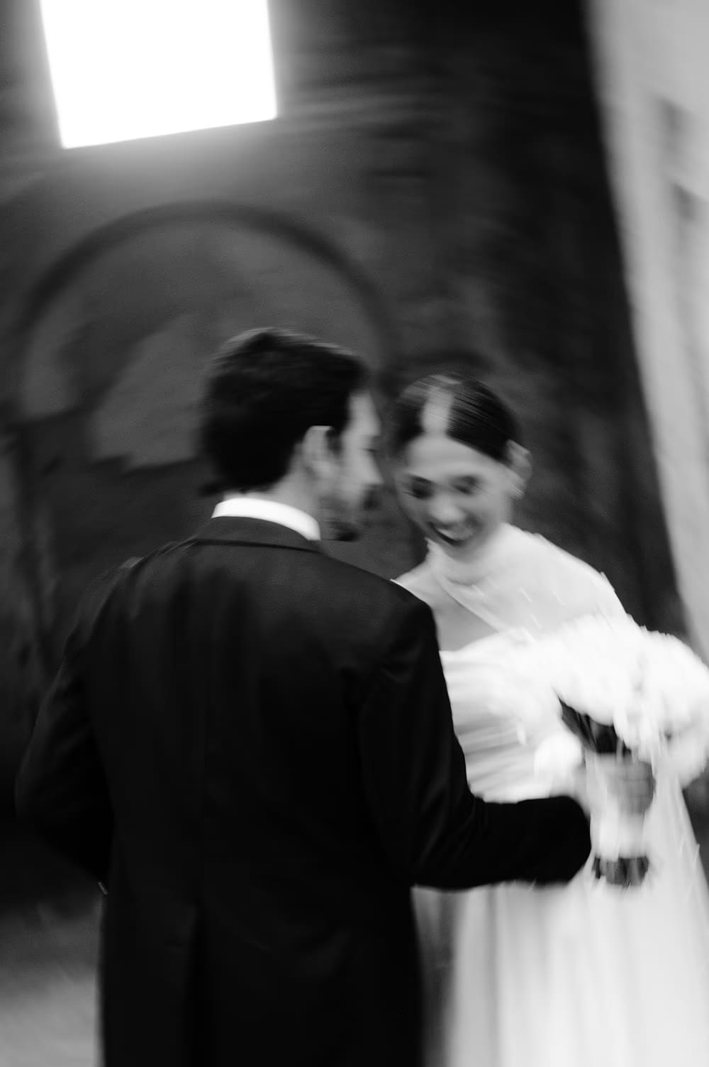 Soft-focus black-and-white moment — groom whispers to the bride beneath a shaft of light inside the cloister at Capuchinas Ruins.