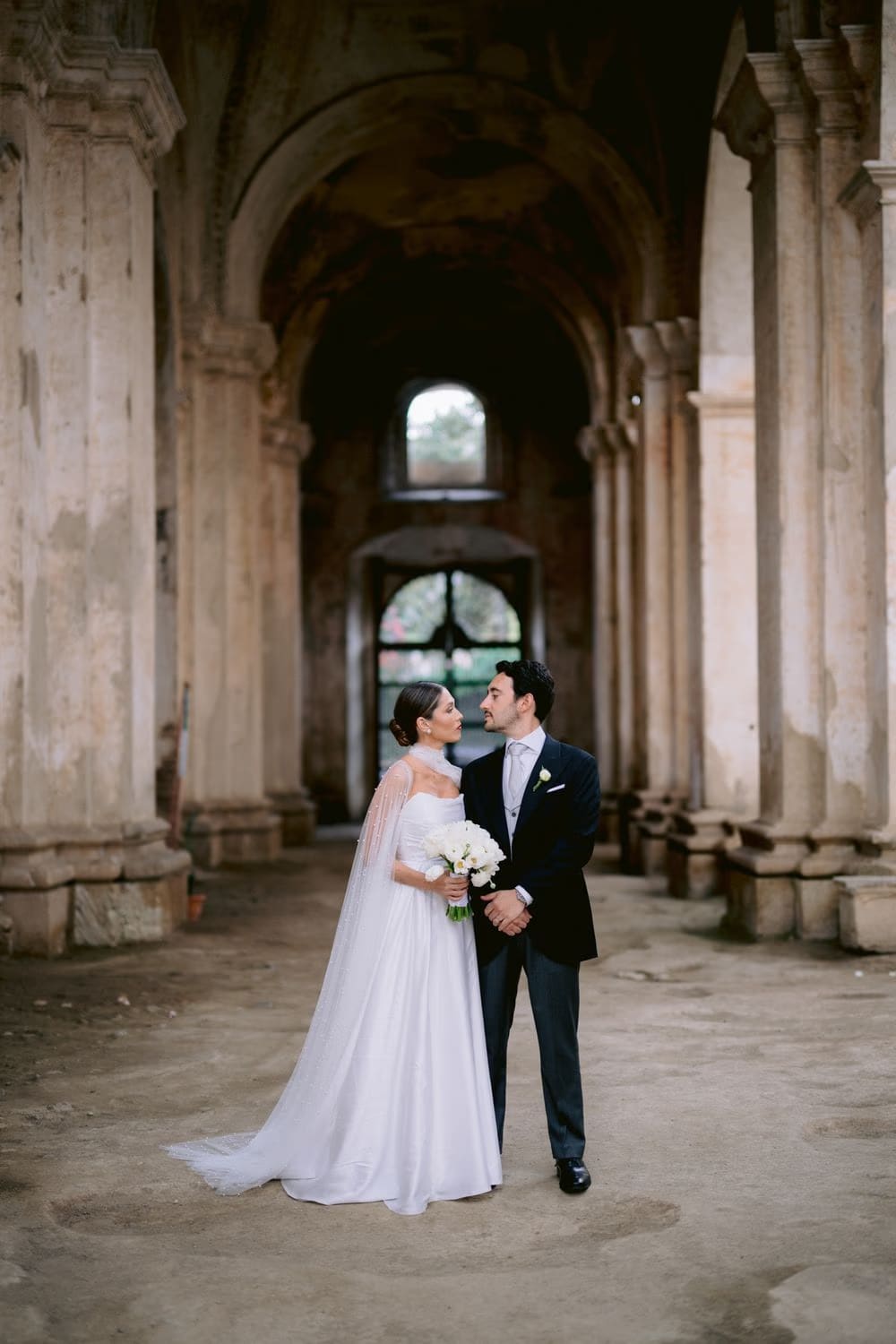 Bride and groom look at each other in the colonnade of Capuchinas Ruins — intimate destination wedding portrait.