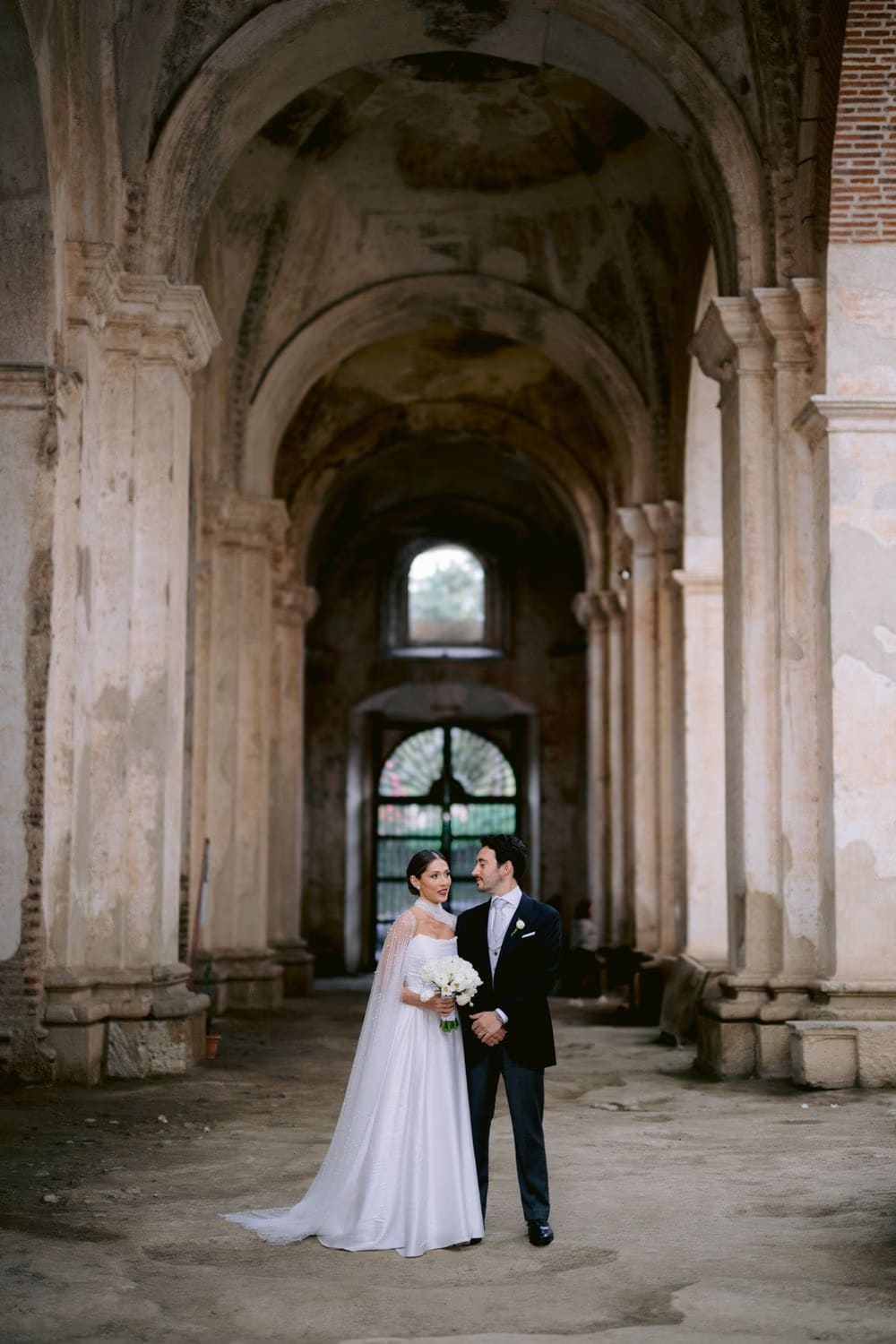 Bride and groom hold hands in the vaulted arcade of the Capuchinas Ruins courtyard — wedding portrait in La Antigua.