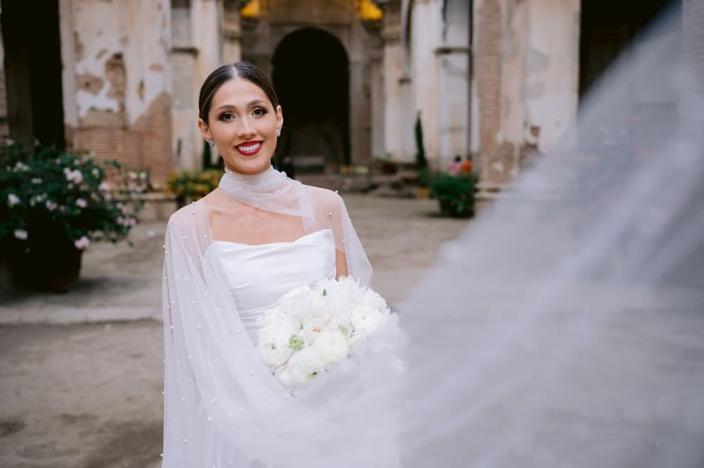 Bride holds her bouquet in the courtyard of Capuchinas Ruins, cape blowing softly in the breeze.