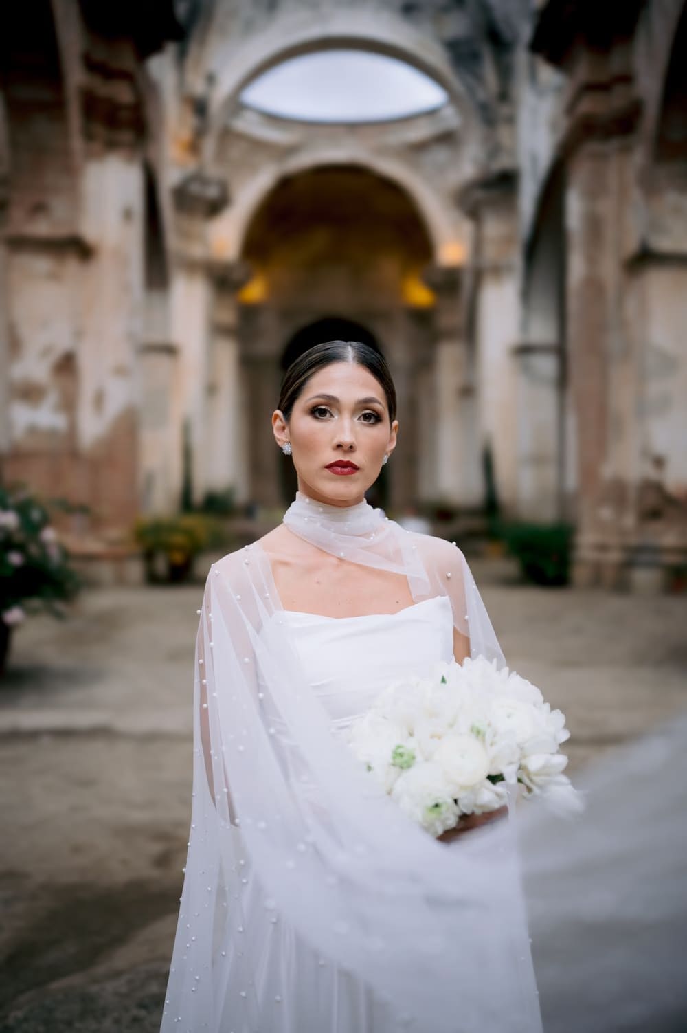 Composed bridal portrait holding her white bouquet centered beneath the dome of Capuchinas Ruins in Antigua Guatemala.