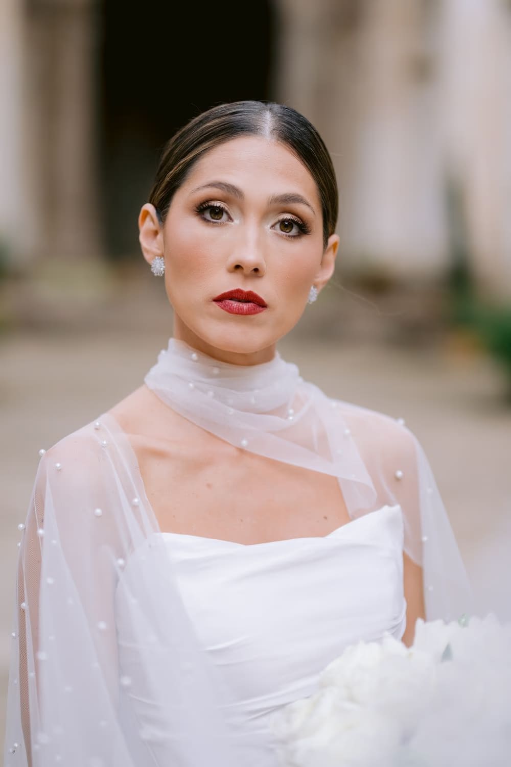 Tight bridal portrait — soft makeup, red lip and pearl-cape neckline against the cloister background in La Antigua.