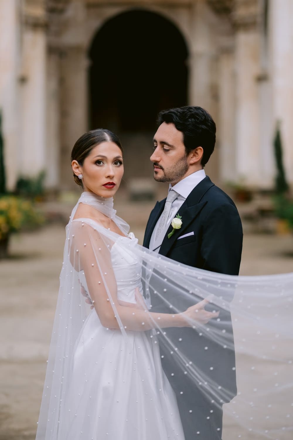 Editorial portrait of the couple as the bride's cape billows around them in the cloister — destination wedding in Antigua.