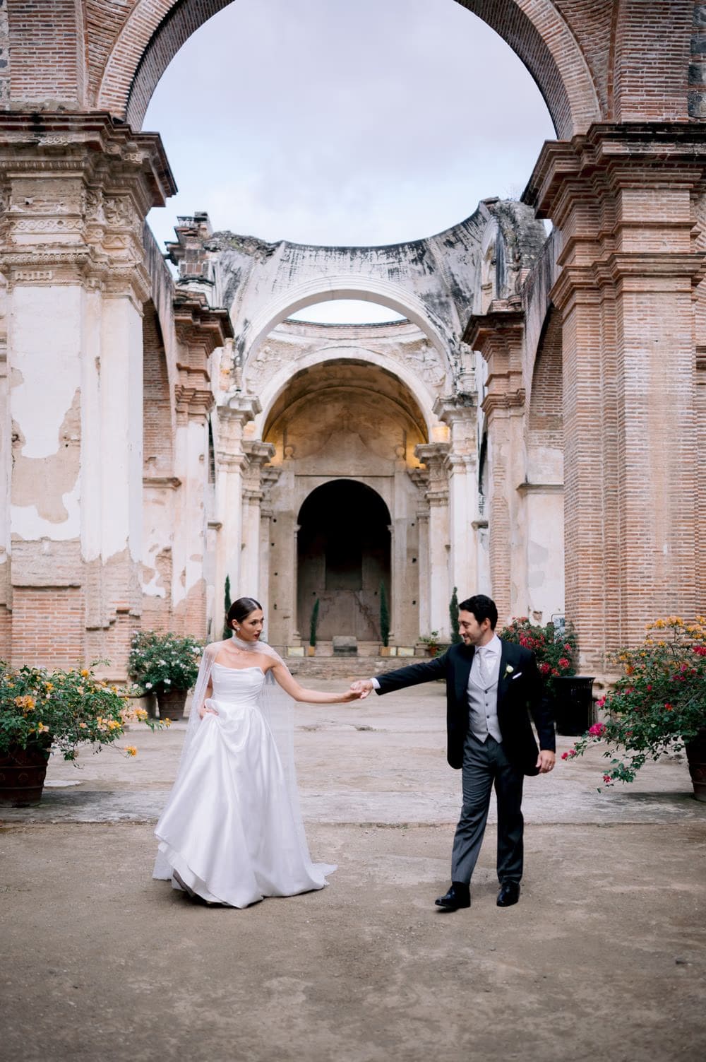 Groom spins his bride with bouquet held high in the long nave of Capuchinas Ruins — joyful destination wedding moment.