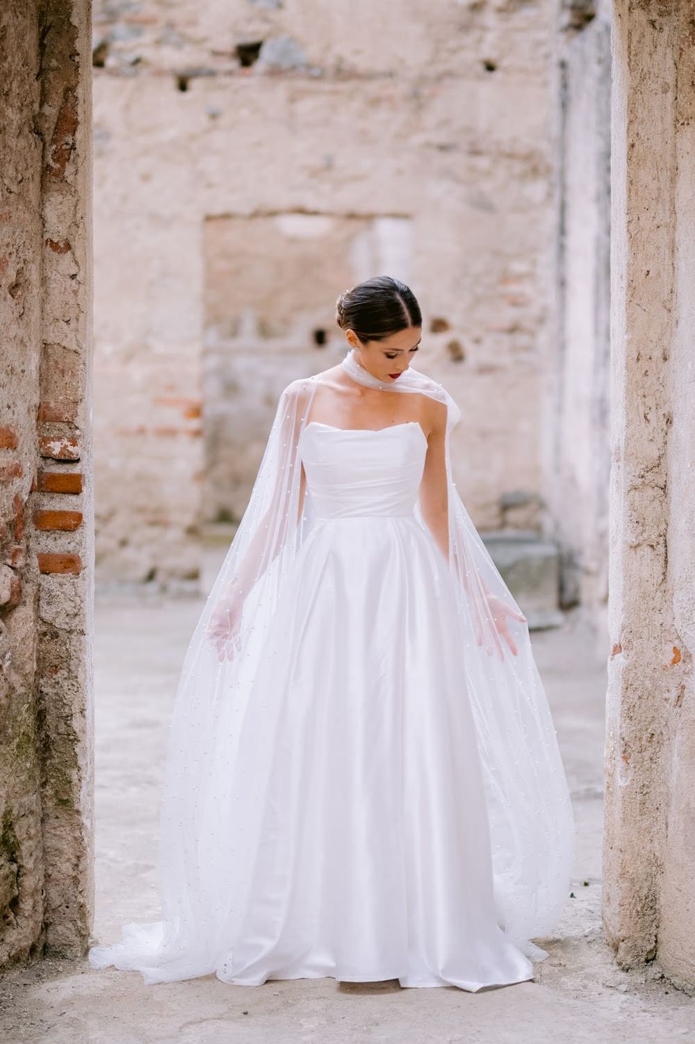 Solo bridal portrait framed inside a weathered stone doorway, full gown and cape on display — Antigua wedding editorial.