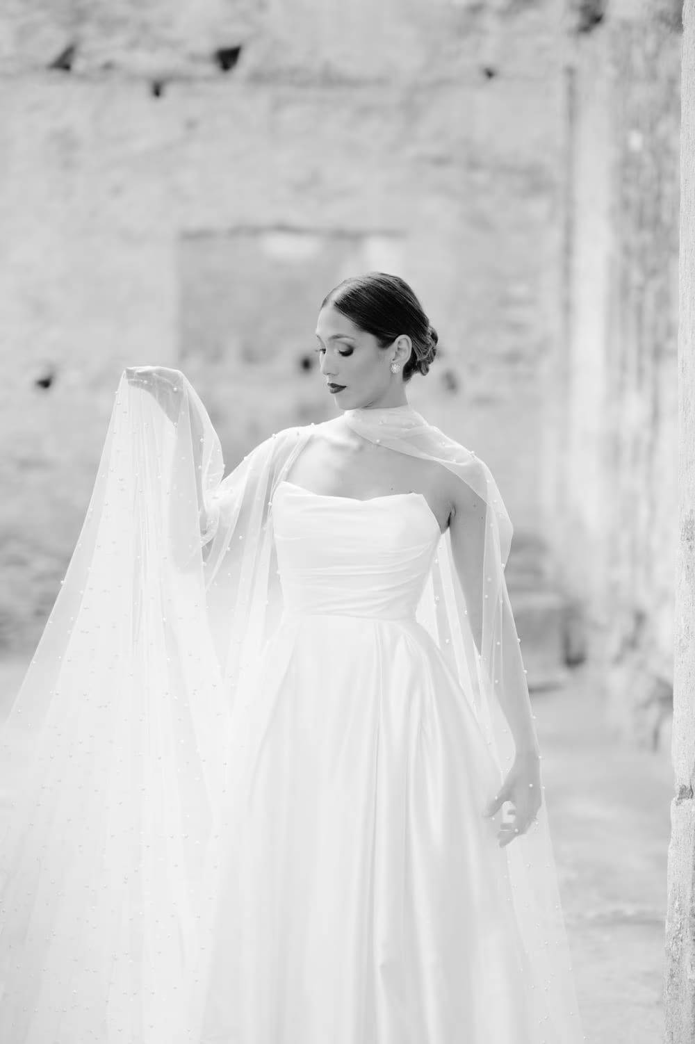Black-and-white bridal portrait — bride lifts cape, gown flowing across the courtyard at colonial Antigua wedding.