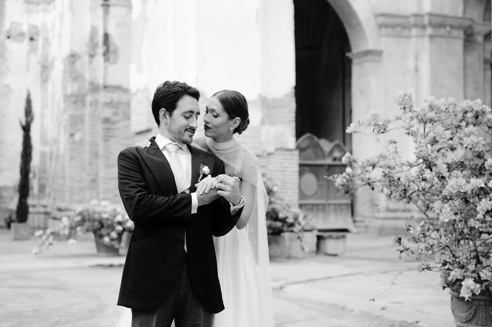 Black-and-white close moment — groom slides the ring onto his bride's finger outside the chapel in colonial Antigua.