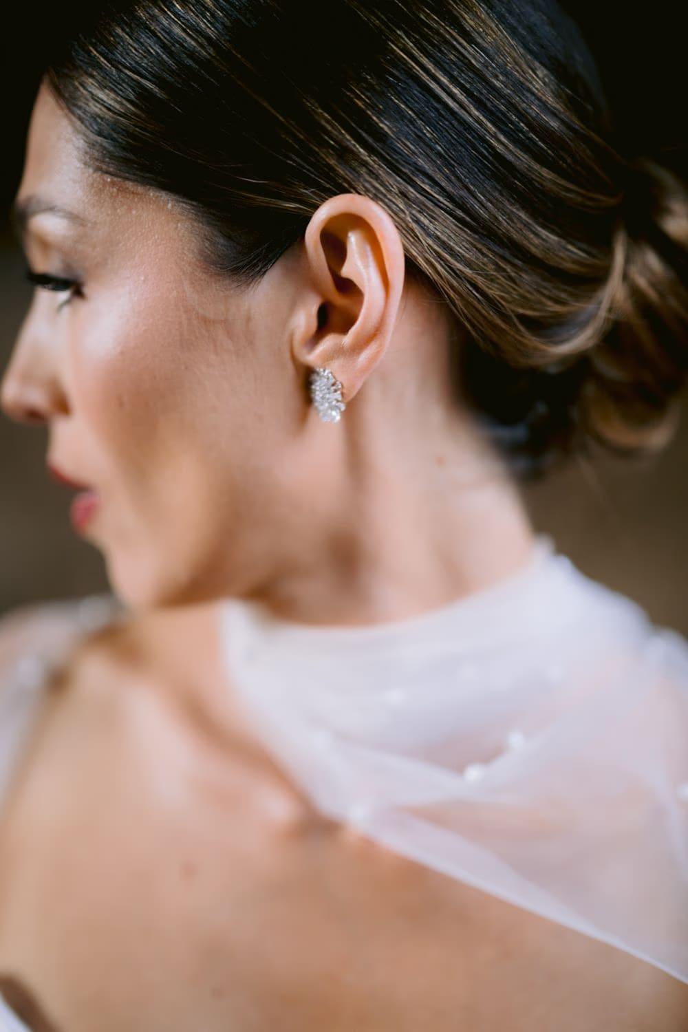 Close detail of the bride's ear with a sparkling cluster earring and slicked low bun — beauty detail in Antigua wedding.