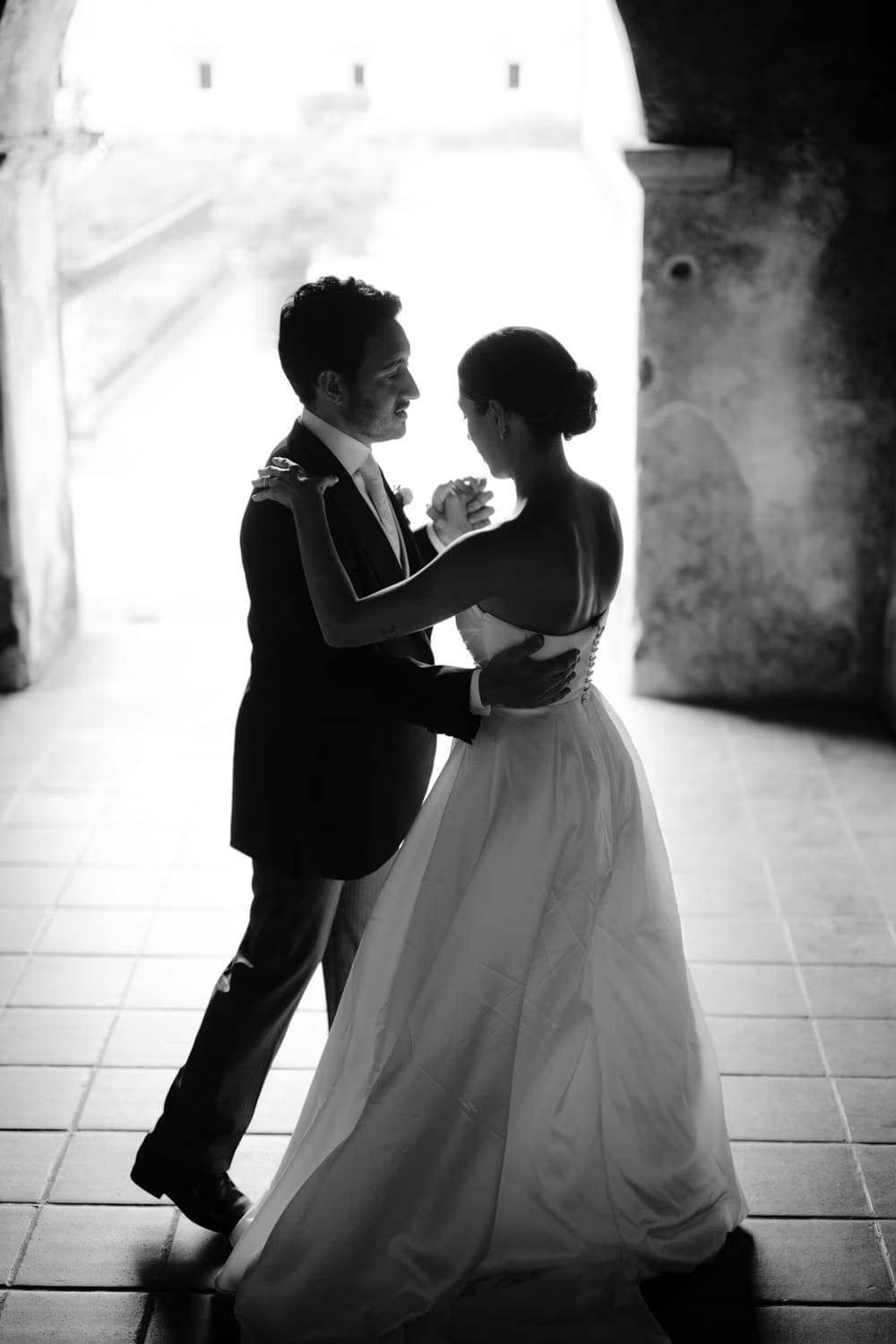 Silhouetted couple embrace beneath an arched passage of Capuchinas Ruins — black-and-white wedding portrait.