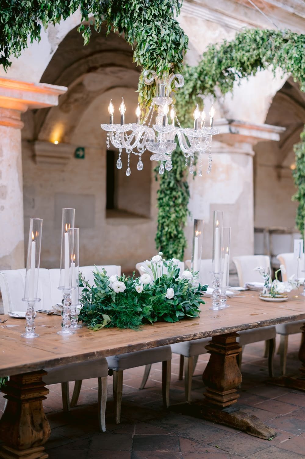 Crystal chandelier hung within cascading greenery above the candle-lit reception table — decor detail at Capuchinas Ruins.