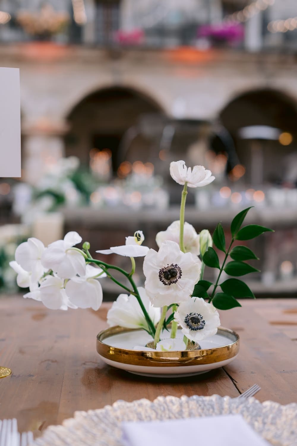 Tabletop centerpiece — white anemones and orchids in a gold dish on the long banquet table — wedding decor detail.