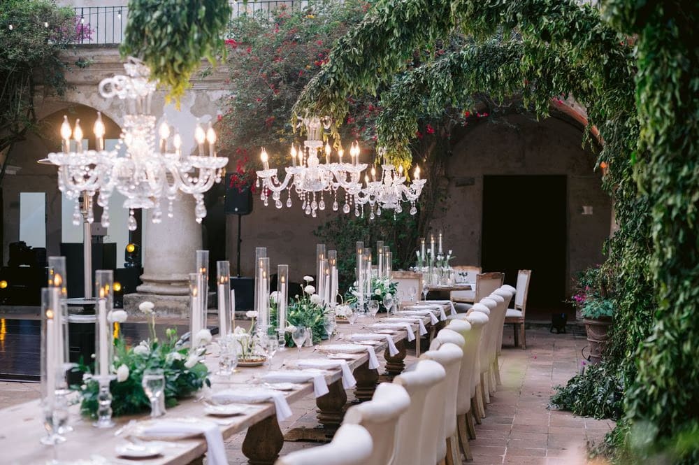 Crystal chandeliers and bougainvillea-draped arches glow over the long reception table — candle-lit wedding dinner setup.
