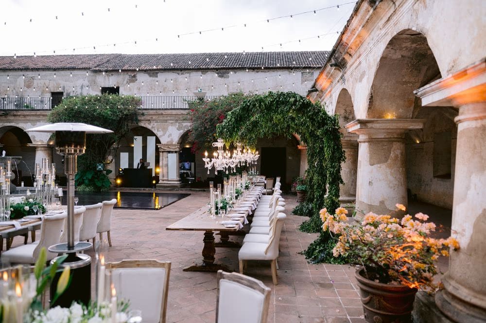Wide reception view — string lights, dance floor and ivy-covered arches surround the dinner setup in the courtyard.