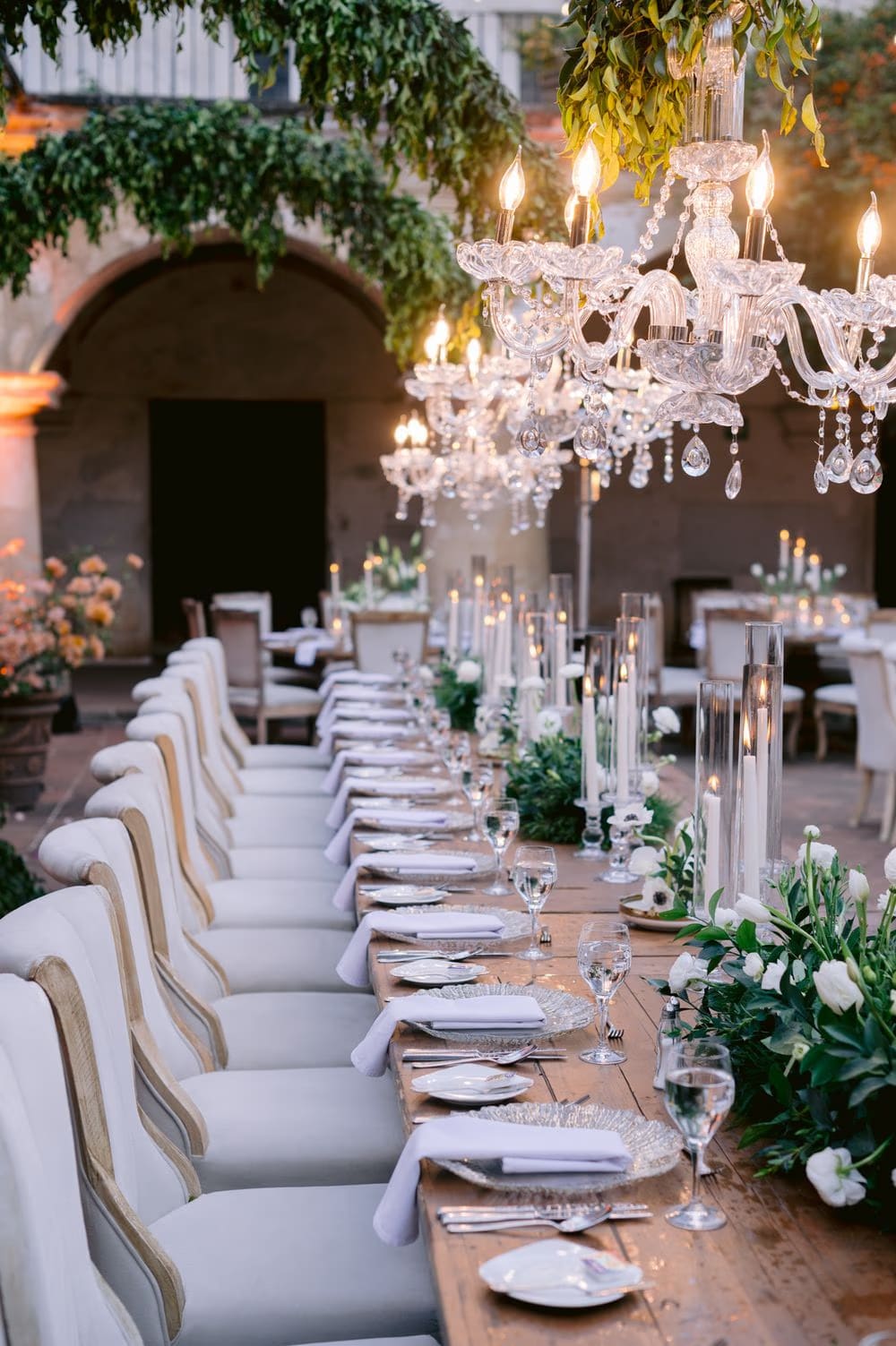 Crystal chandelier and tall tapers run the length of the wedding table set with greenery — reception detail at La Antigua.