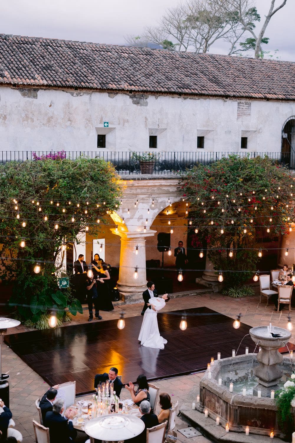 Aerial view of the first dance — bride and groom alone on a wooden dance floor strung with bistro lights at Capuchinas Ruins.