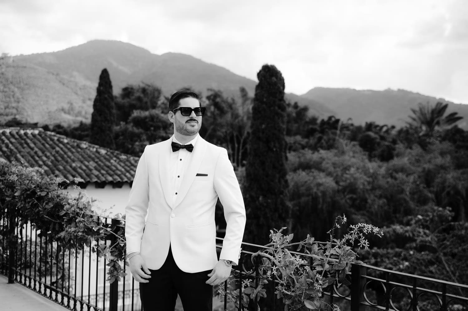 Black-and-white groom portrait in white tuxedo with volcano backdrop — Antigua wedding photography.