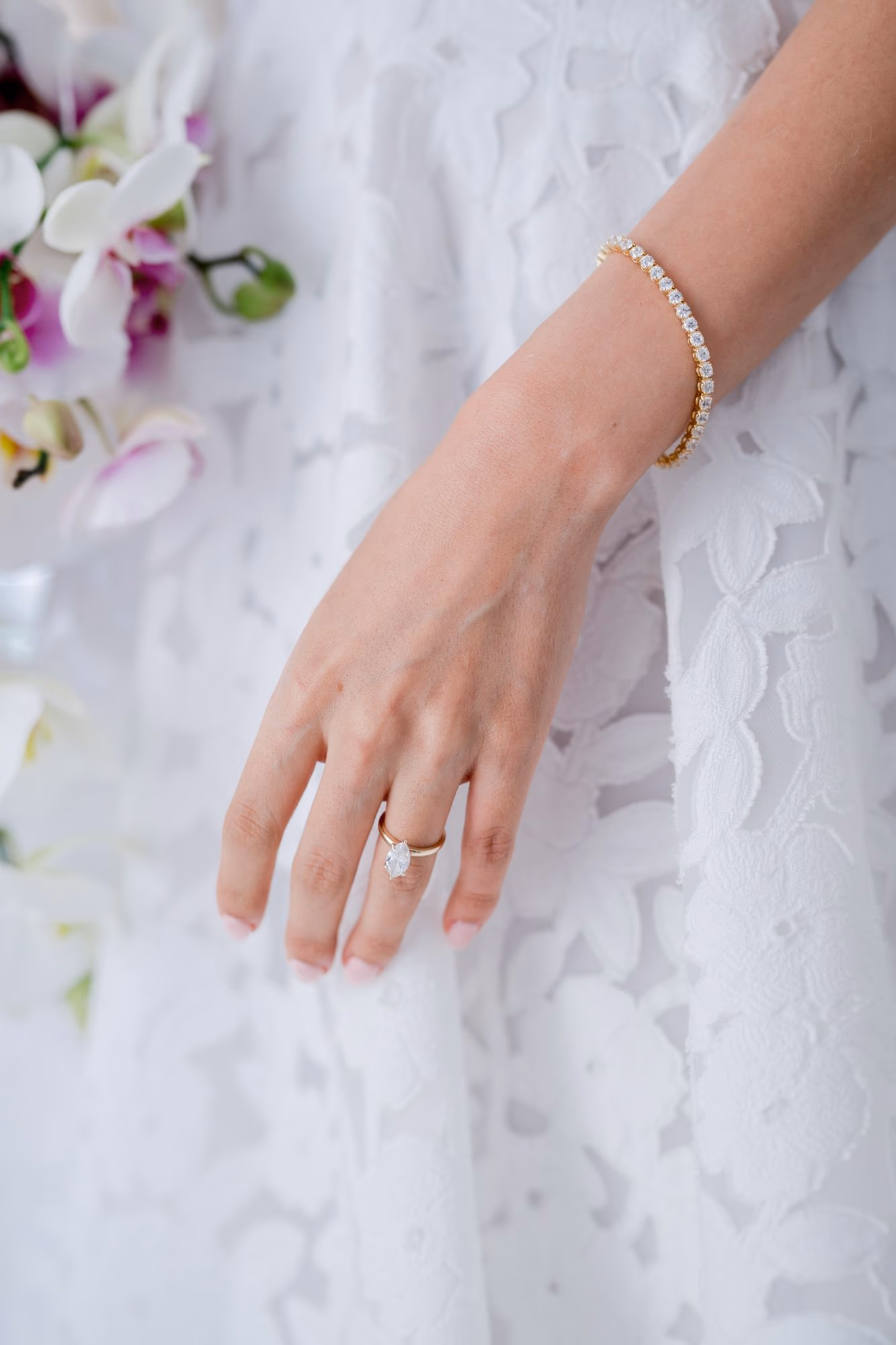 Engagement ring and gold tennis bracelet on the bride's hand resting on a lace dress — wedding detail in Antigua Guatemala.