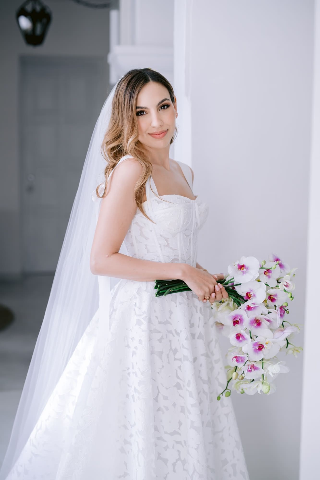 Bridal portrait in cathedral veil holding an orchid bouquet — soft window light at Villa Bokeh.