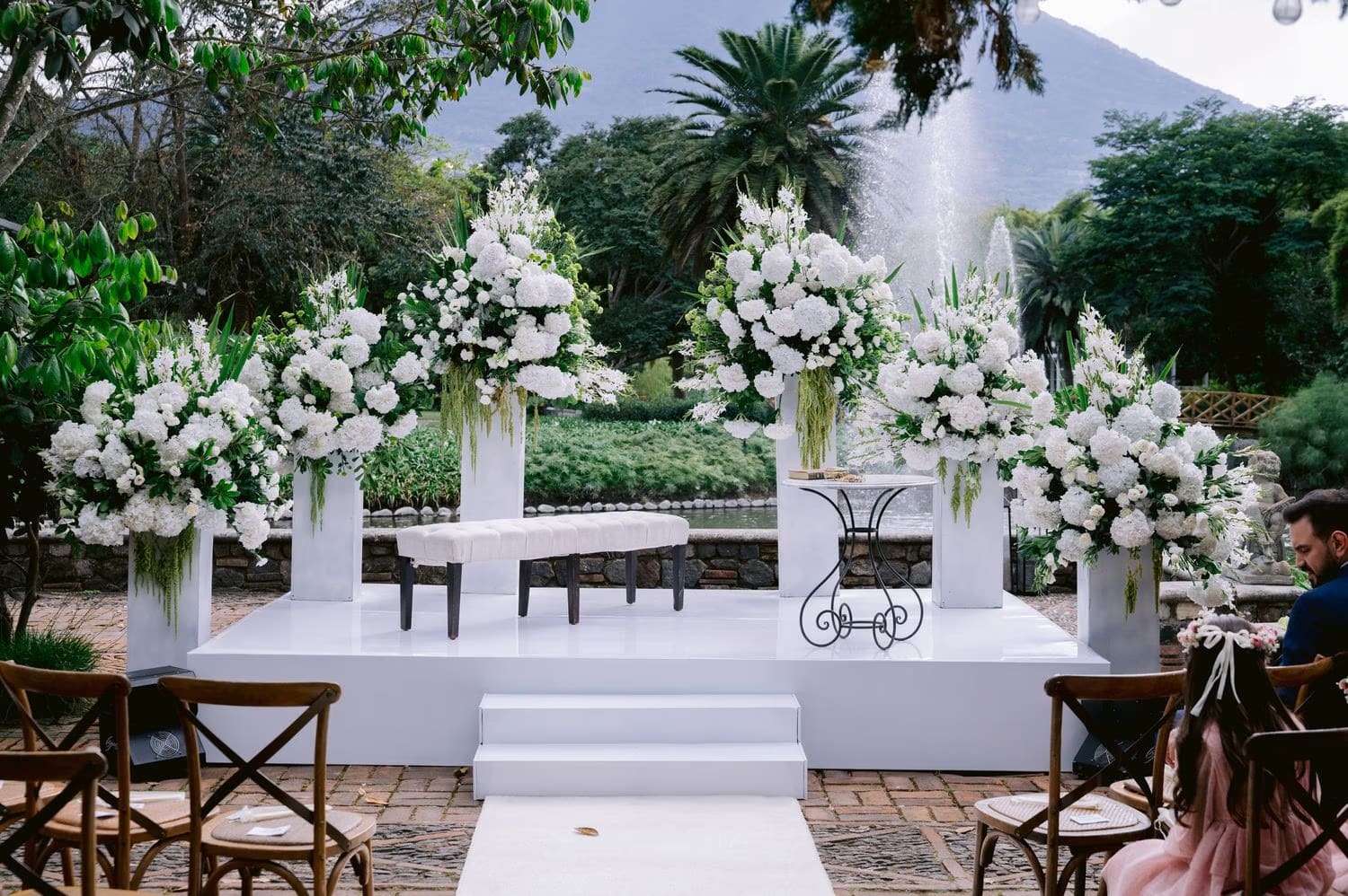 Empty ceremony altar with towering white floral arrangements and the lagoon fountain rising behind.