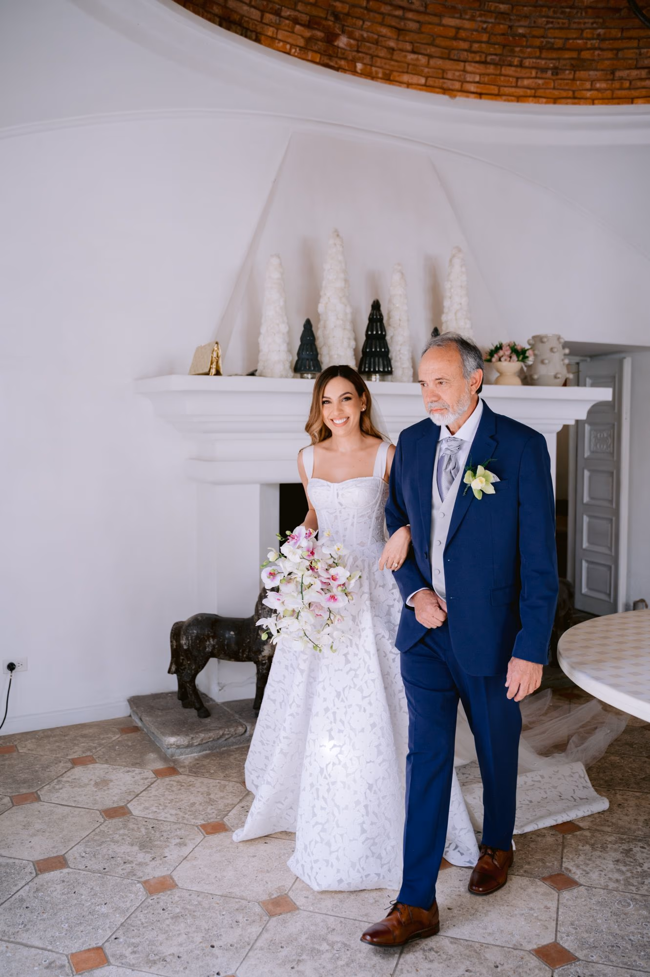 Caro stands arm-in-arm with her father inside a domed brick salon at Villa Bokeh just before walking down the aisle.
