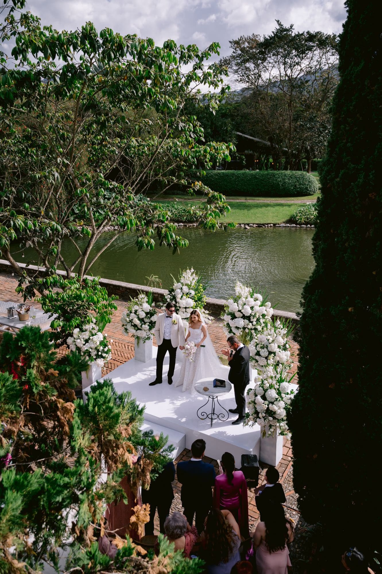 Ceremony seen from across the lagoon, white florals framing the couple at the altar — Villa Bokeh wedding.
