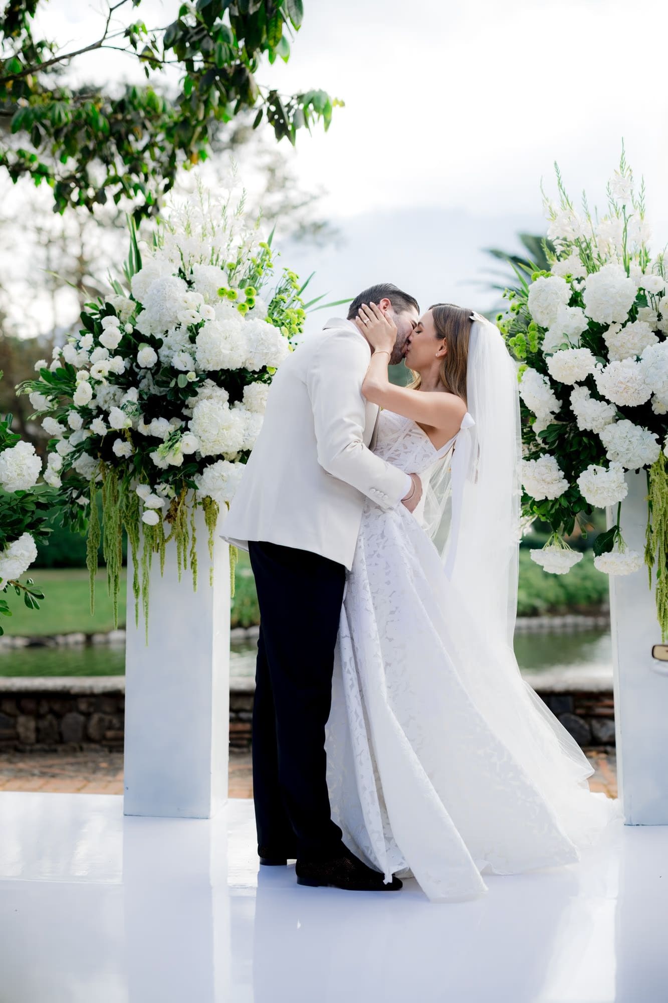 Bride and groom share their first kiss as a married couple beneath cascading white florals at Villa Bokeh.