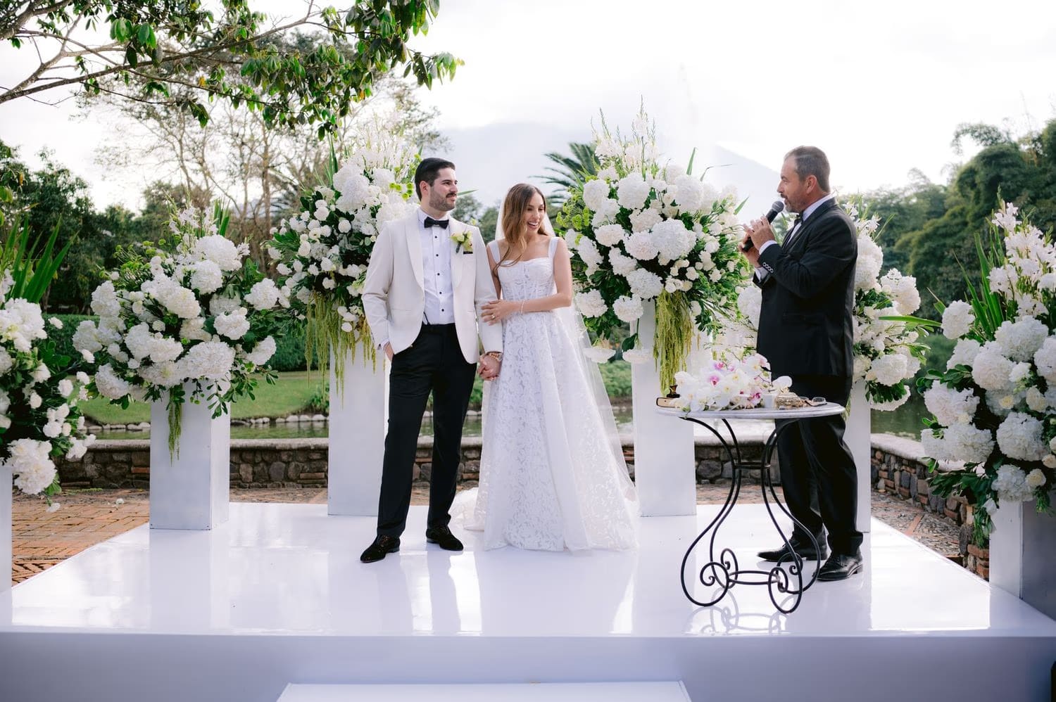 Officiant blesses the couple at the floral altar as guests look on — Villa Bokeh ceremony.
