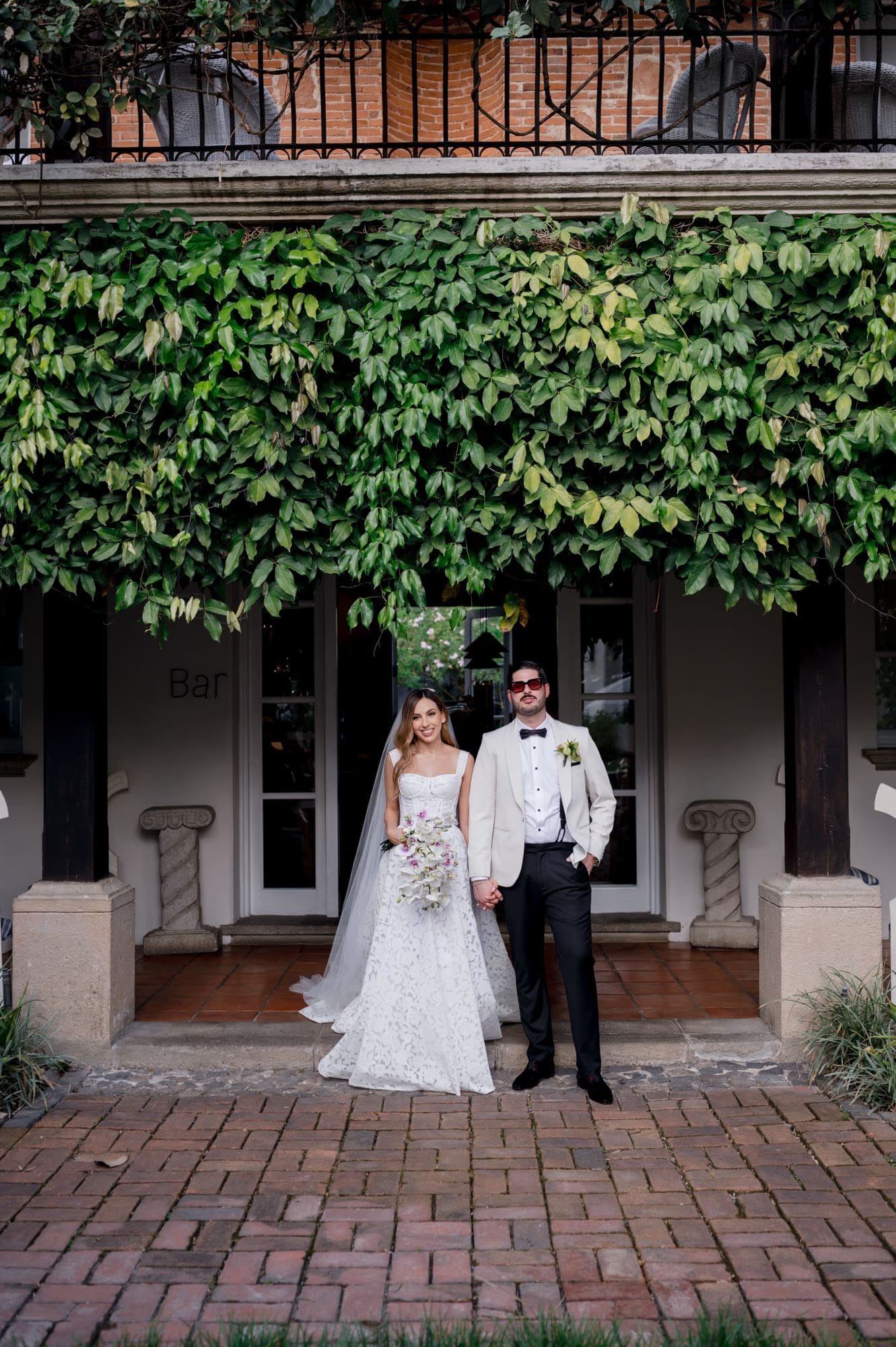 Couple poses under a hanging curtain of green vines by the bar at Villa Bokeh — intimate wedding portrait.