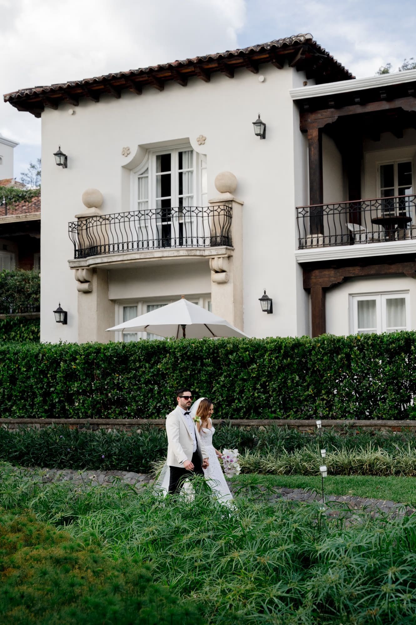 Newlyweds walk past a colonial villa with tiled balconies — destination wedding in Antigua Guatemala.