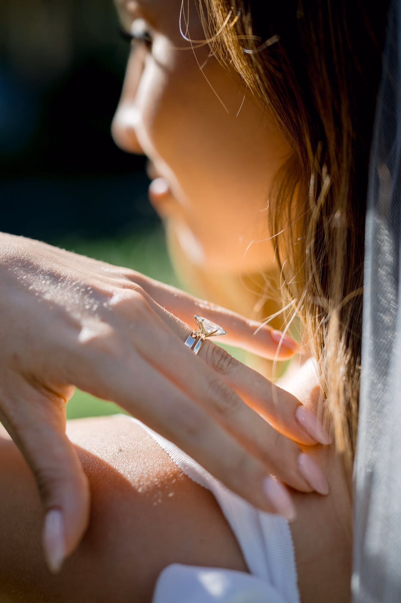 Close-up of the diamond engagement ring on the bride's hand resting on her shoulder — wedding detail.