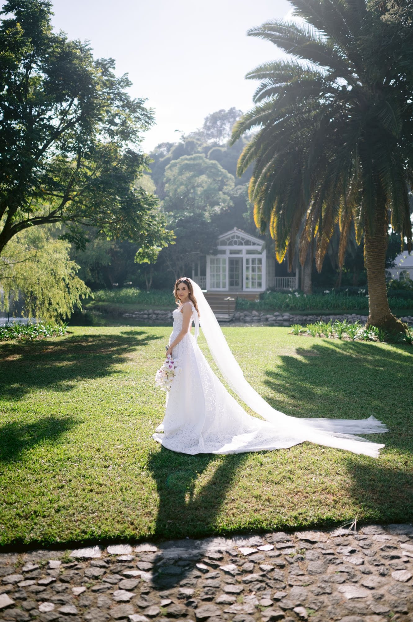 Wide bridal portrait under palms with the lakeside garden house behind — Villa Bokeh wedding.