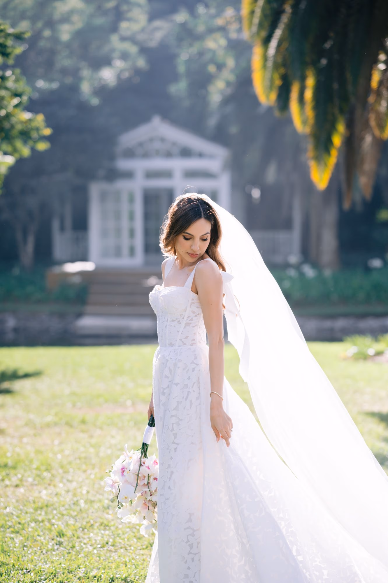 Bride looks down toward her bouquet on a sunlit lawn — soft bridal portrait at La Antigua.