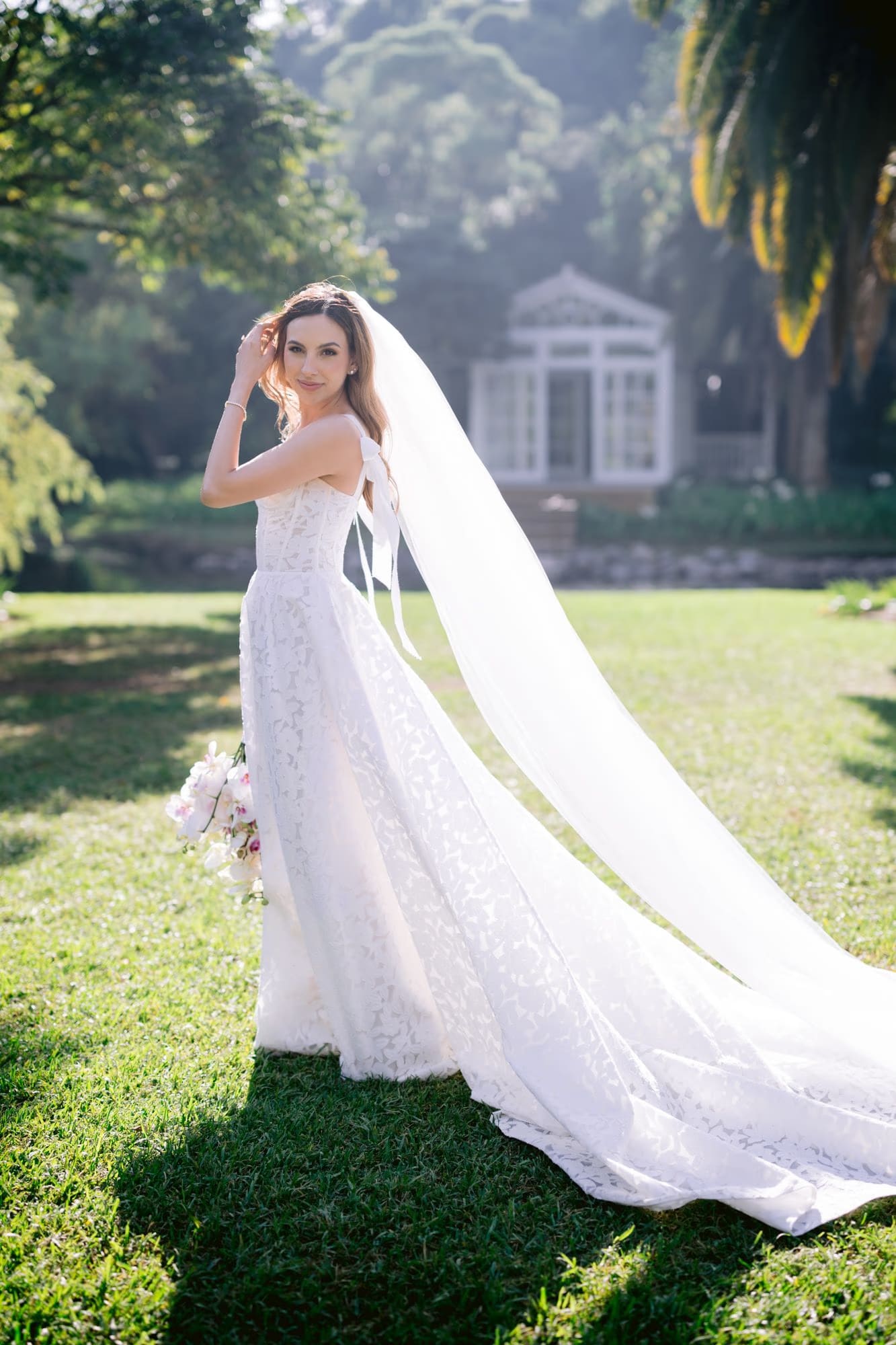 Caro turns toward camera, veil drifting in the wind across the garden lawn at Villa Bokeh.