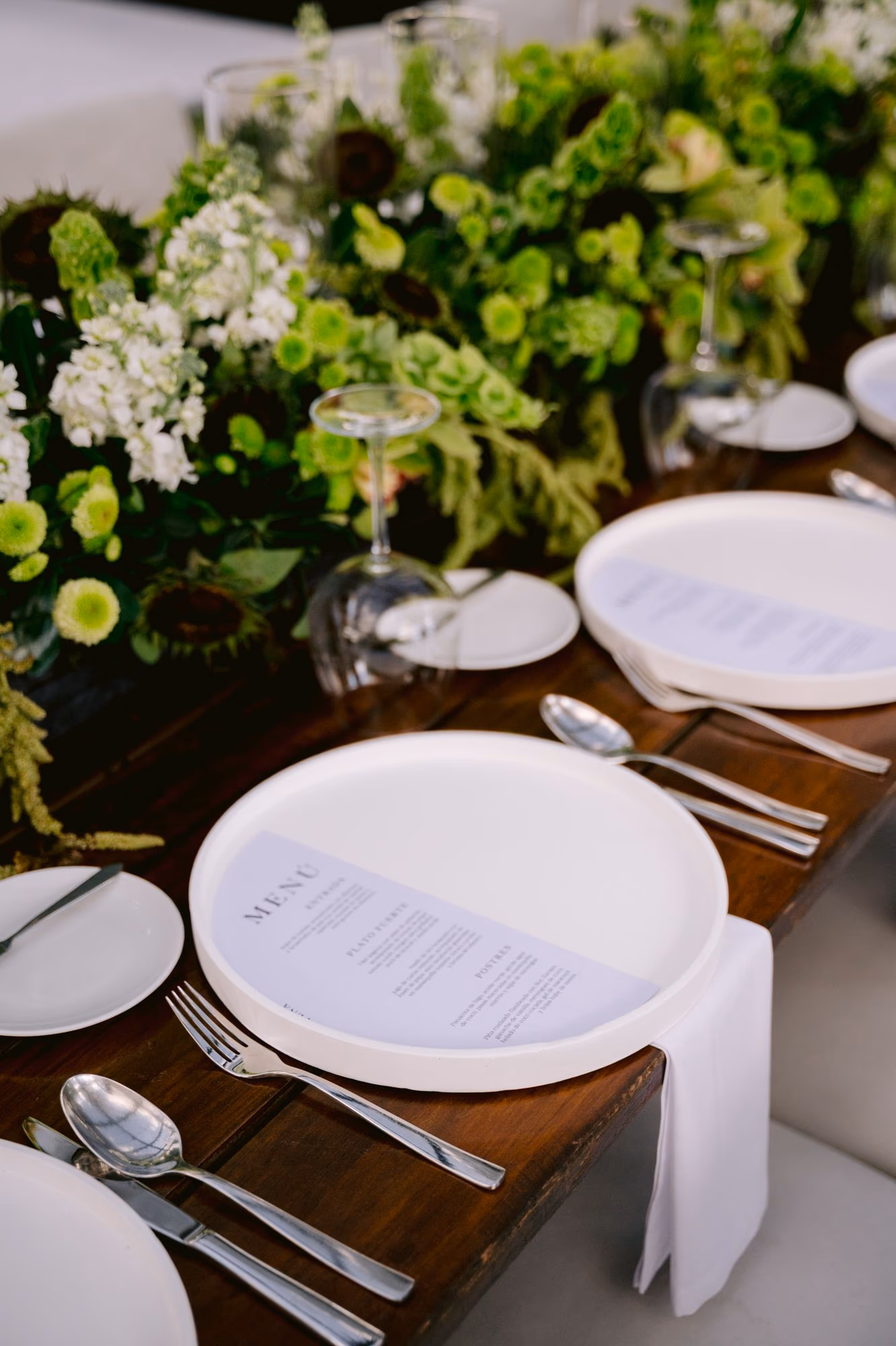 Place setting with printed menu, white plate and green floral runner — reception detail at Villa Bokeh.