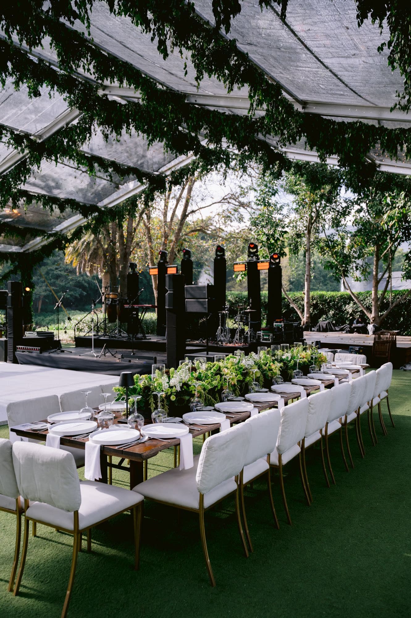 Wide reception view under the clear tent with stage, band setup and long dinner table.